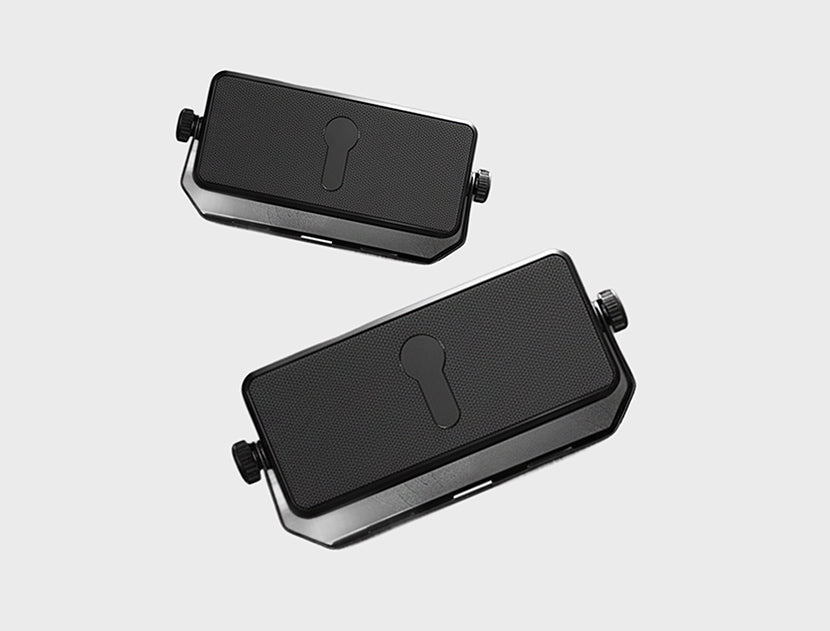 Two black rectangular electronic components with textured tops, keyhole-shaped cutouts, and small side knobs, shown on a light gray background.